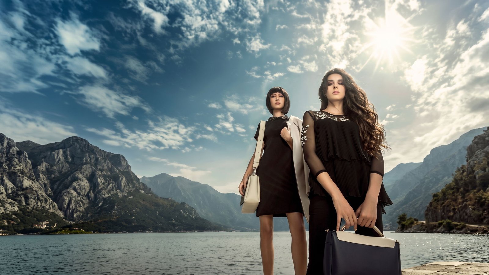 Two models with leather handbags photographed against mountains and water