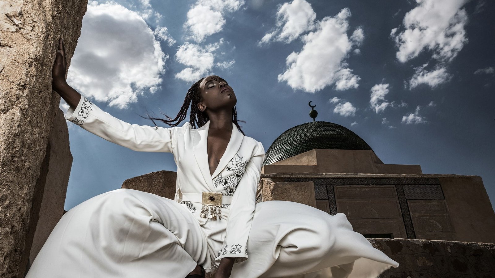 White embroidered suit photographed against a domed roofline and open sky
