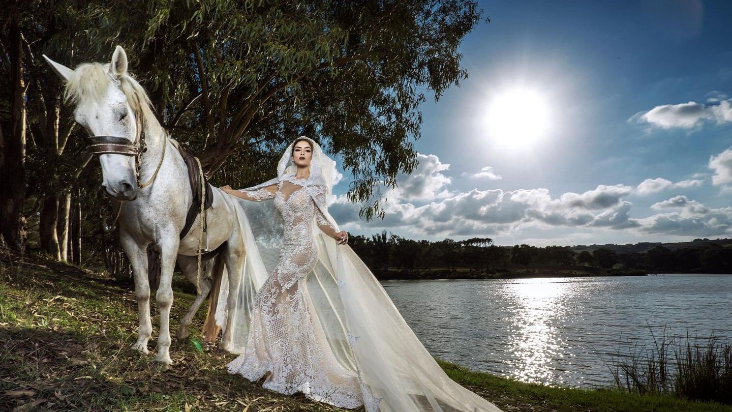 Lace bridal gown with a long veil photographed beside a lake