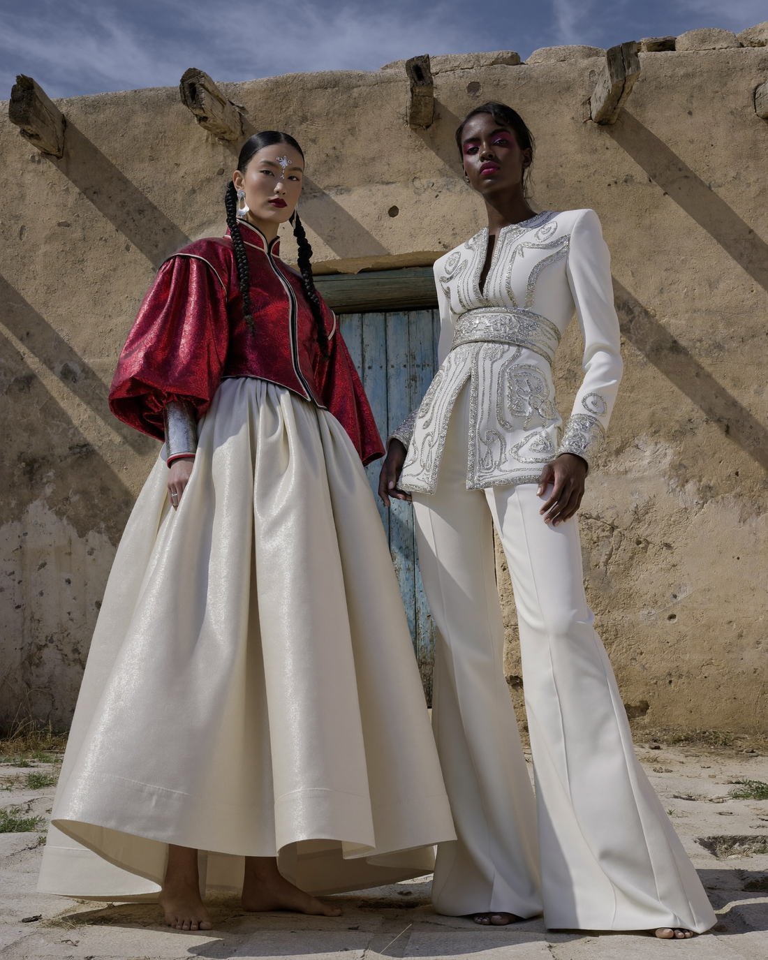 Two models in white couture at a mud-brick wall, Daughter of the Wind