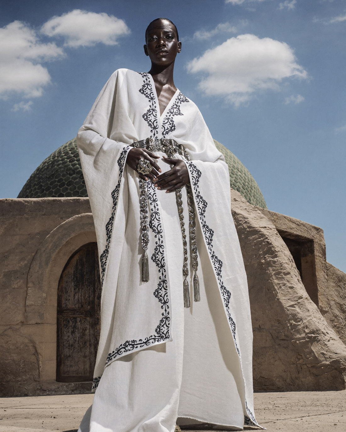 Embroidered white robe at a domed entrance, Daughter of the Wind