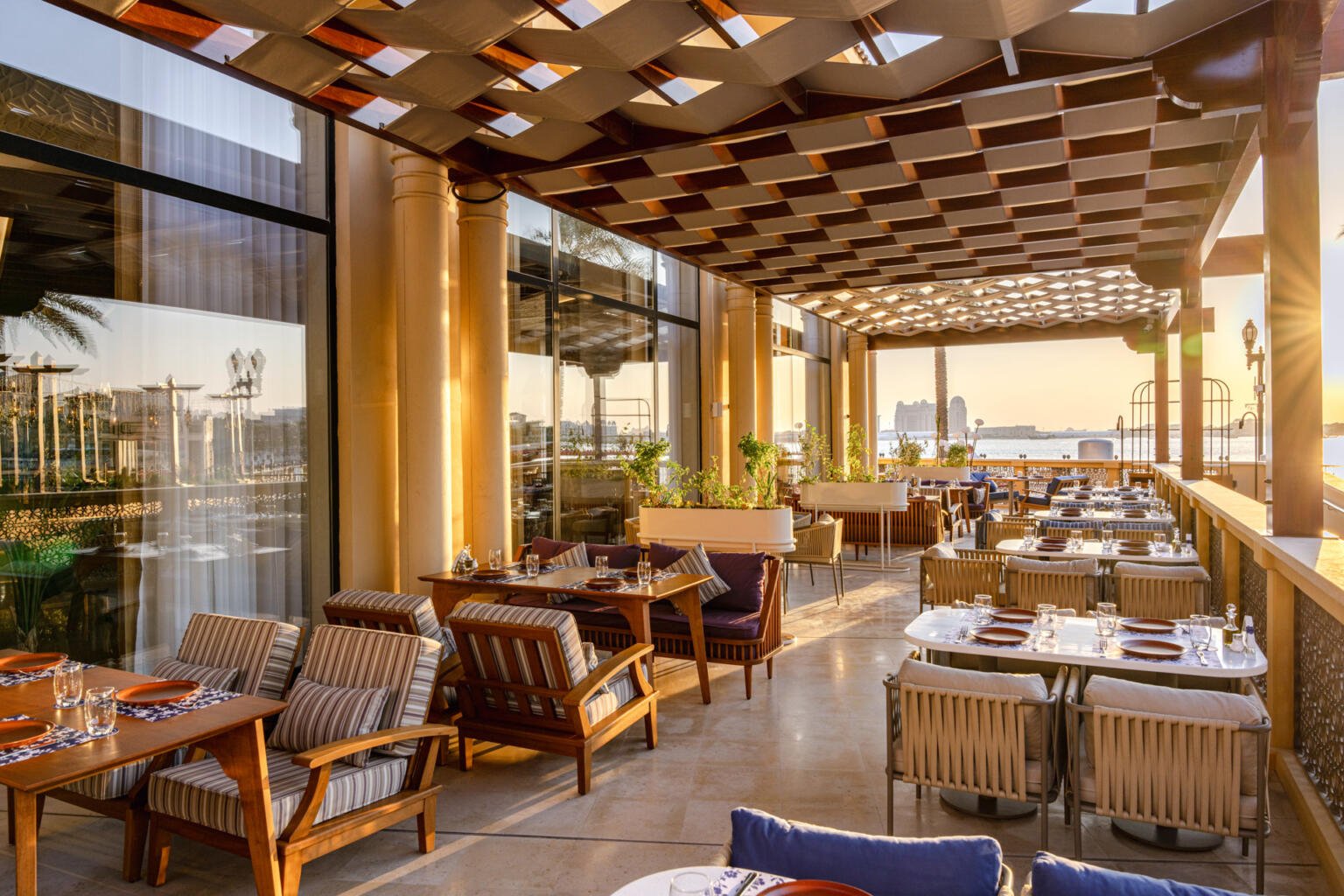 Loris terrace seating at golden hour under the timber lattice roof, sea and palm in view
