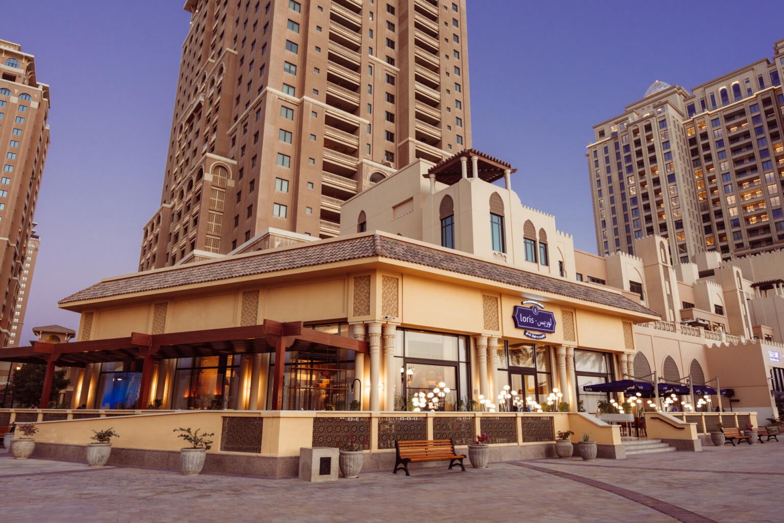 Exterior of Loris restaurant in Doha with its signage, palms and a car passing in late afternoon light