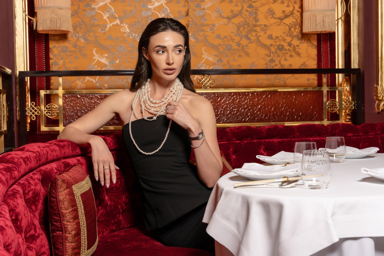 Model on a red banquette beside a set table, restaurant lifestyle photography Doha
