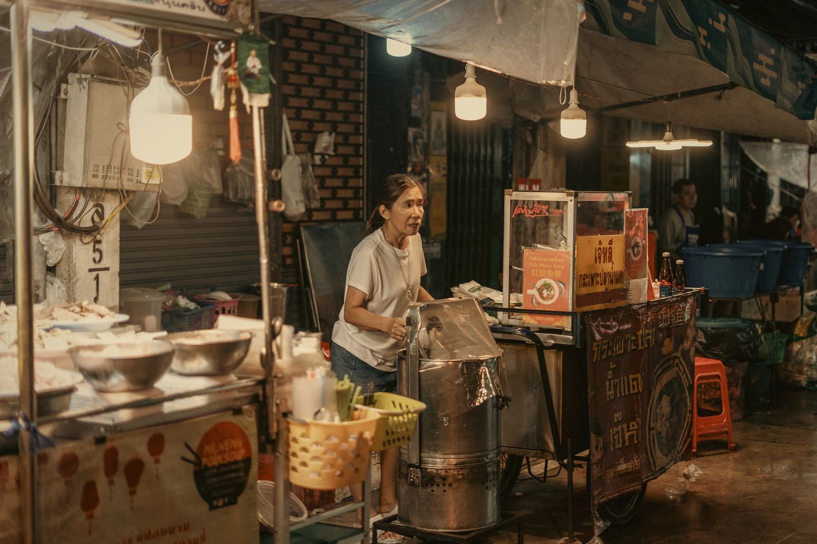 A street food cook under a bare bulb in Bangkok, Thailand