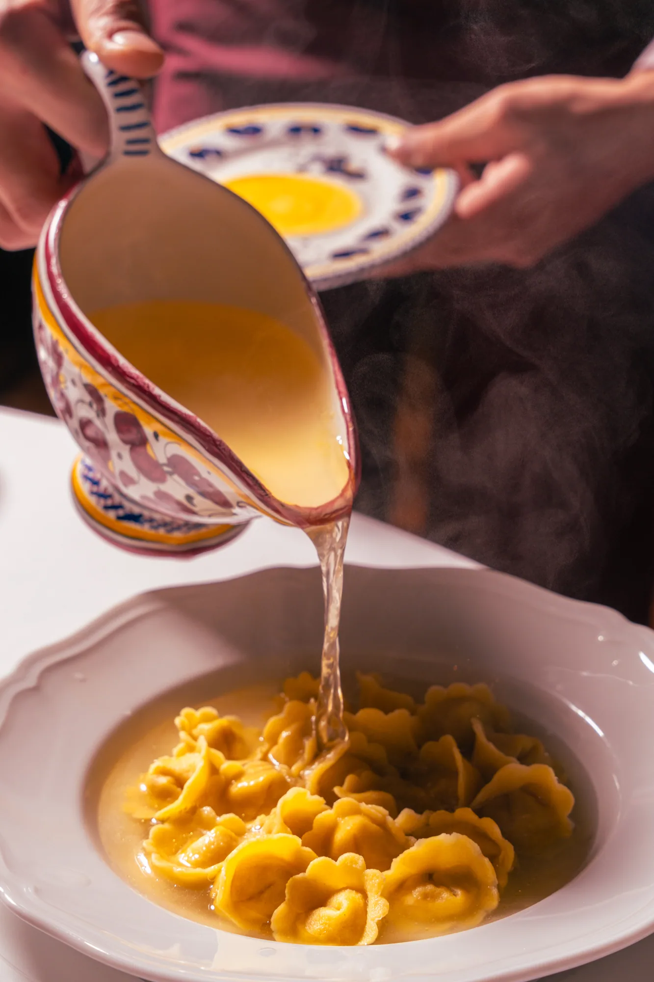 Tortellini in brodo being poured at the table at Carbone Doha, captured mid-pour