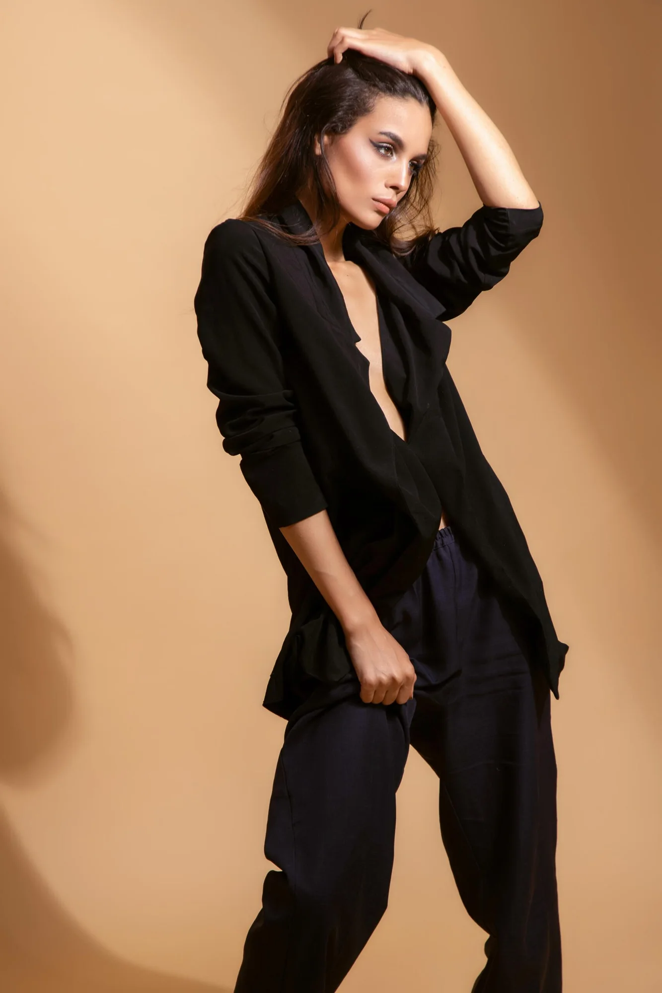 Model in a black trouser suit against a warm beige studio backdrop