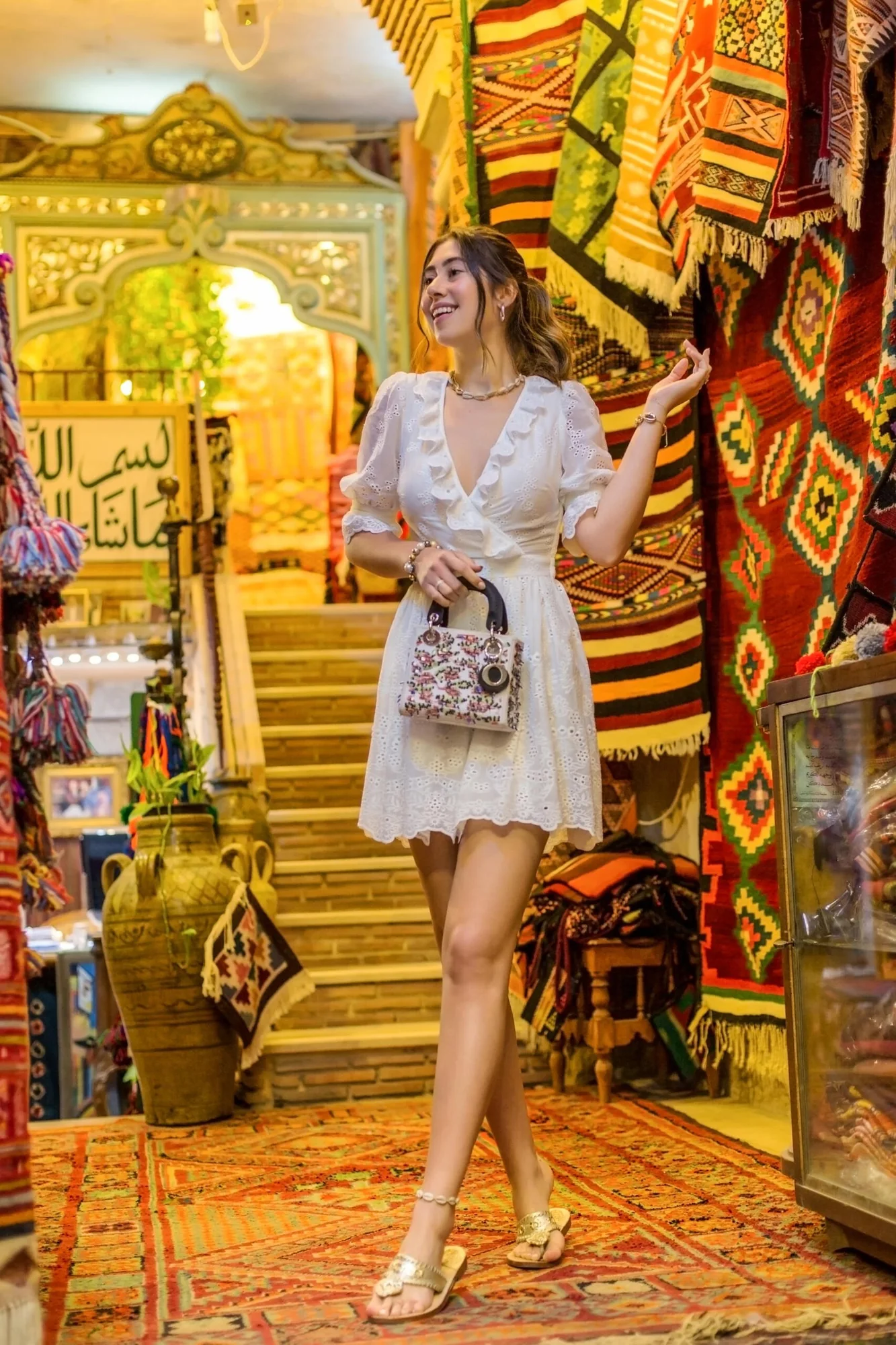 Model in a white dress on steps surrounded by colourful textiles and lamps