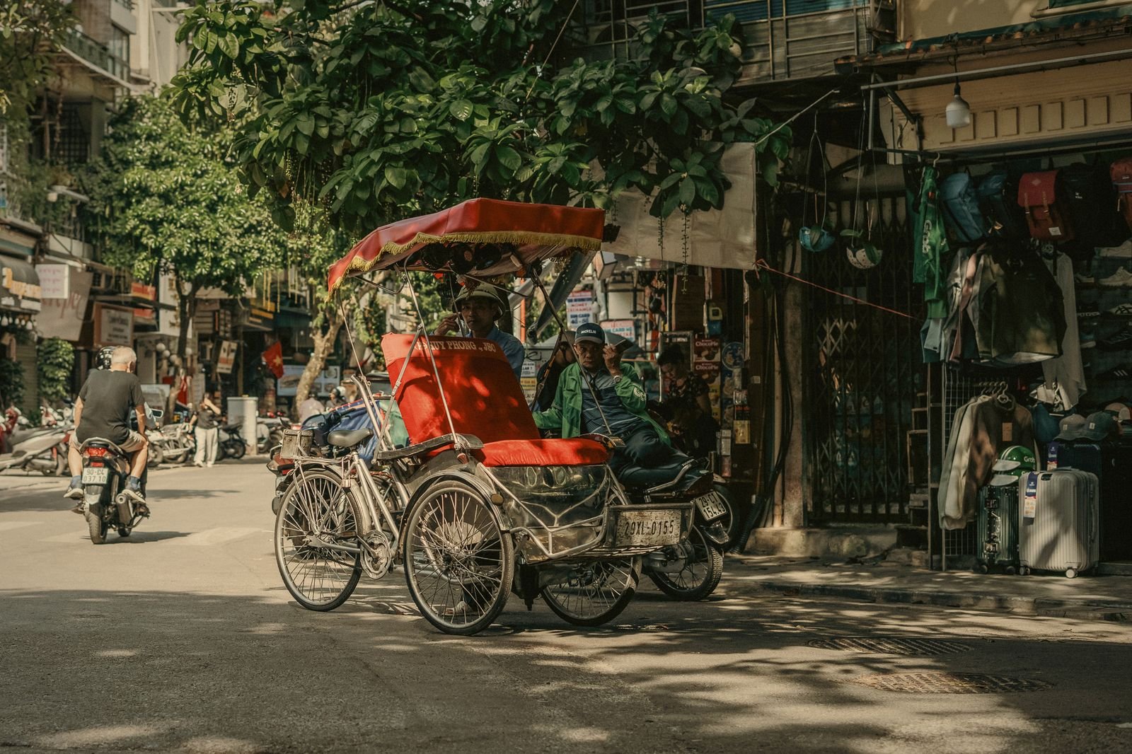 A cyclo rolling through a tree-lined Hanoi street