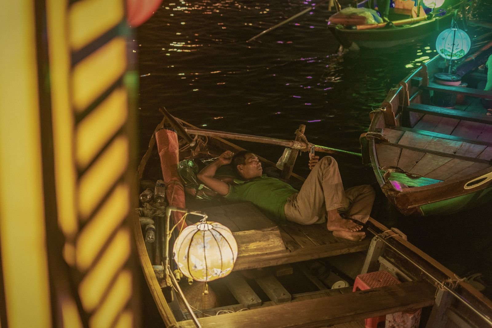 A boatman resting in his lantern-lit boat on the Thu Bon river, Hoi An