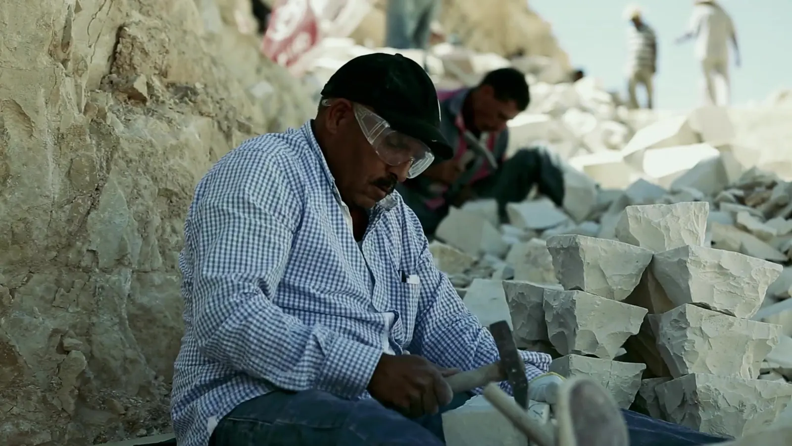 Decent Work, Up Close: ILO Documentary Films 4 A stone worker in a cap shaping a block of pale stone at an open-air quarry