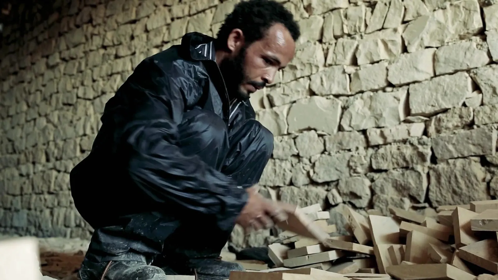 Decent Work, Up Close: ILO Documentary Films 10 A young man in a dark jacket cutting stone beside a dry stone wall
