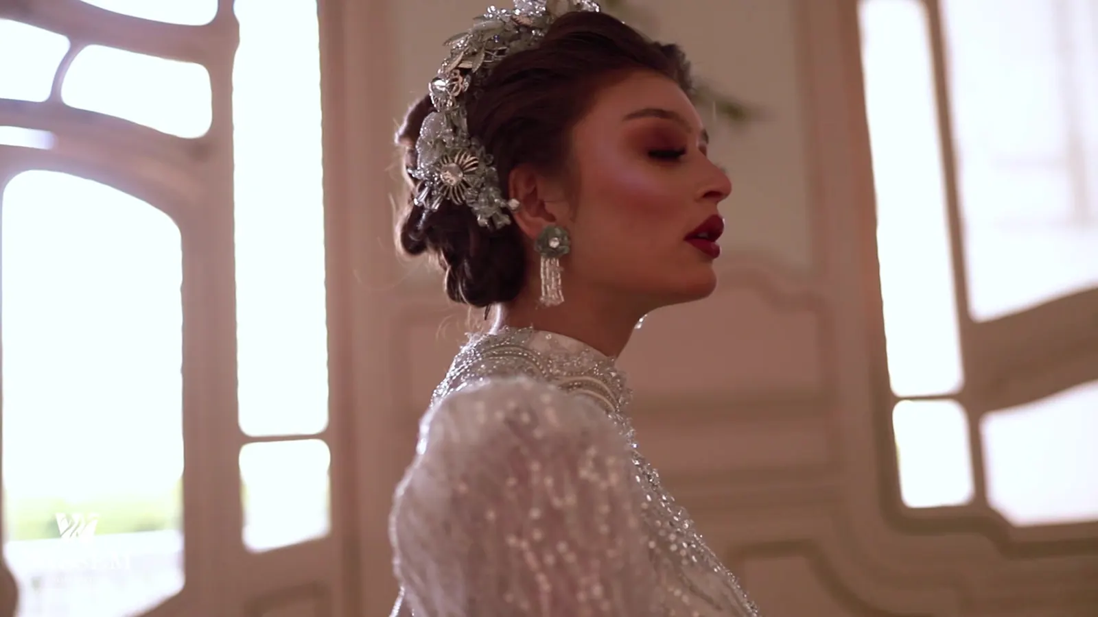 Bride in profile beside an arched window wearing a jewelled hair piece
