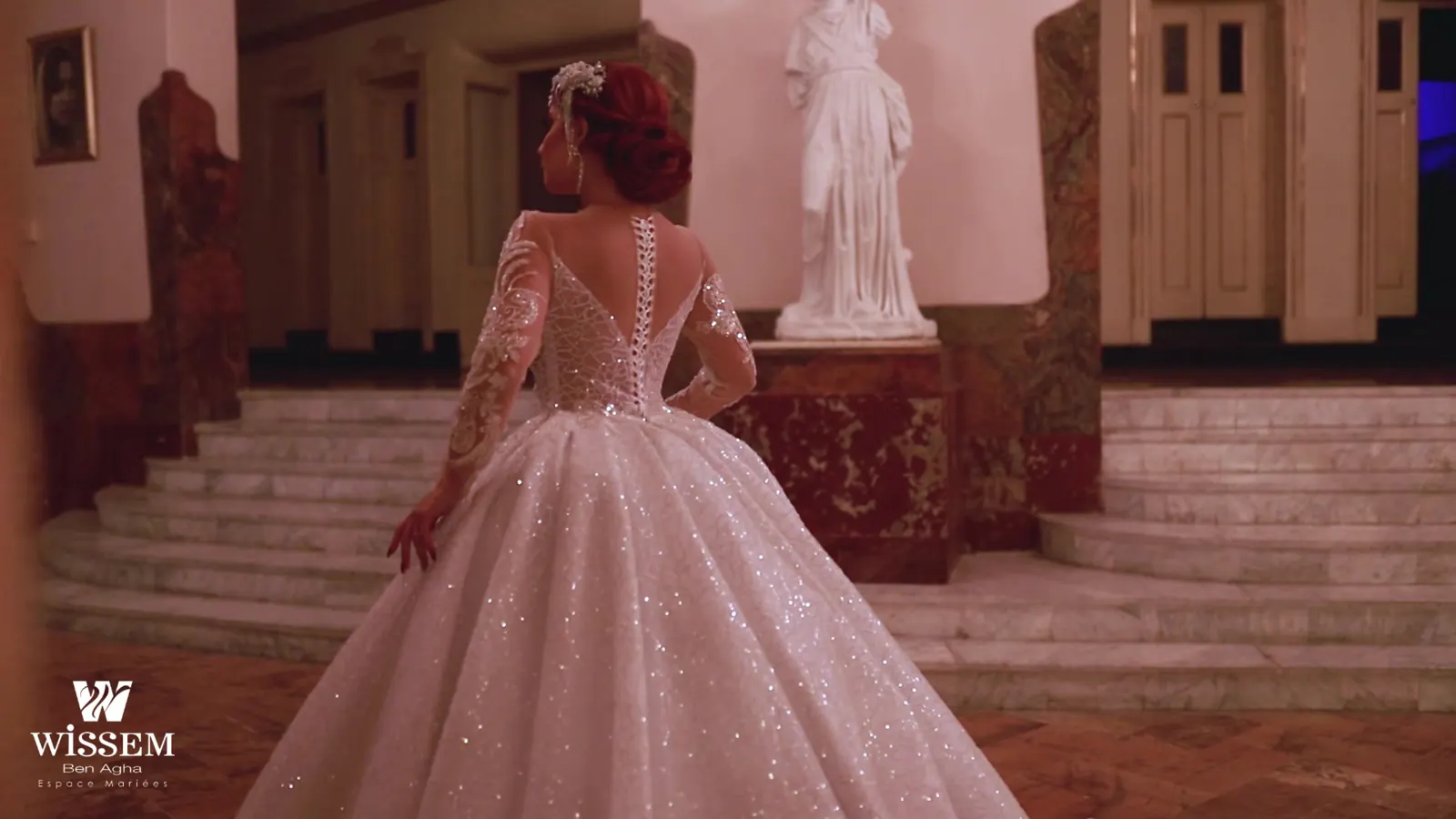 Bride in a full sequinned ball gown descending a marble staircase with a dark wooden banister