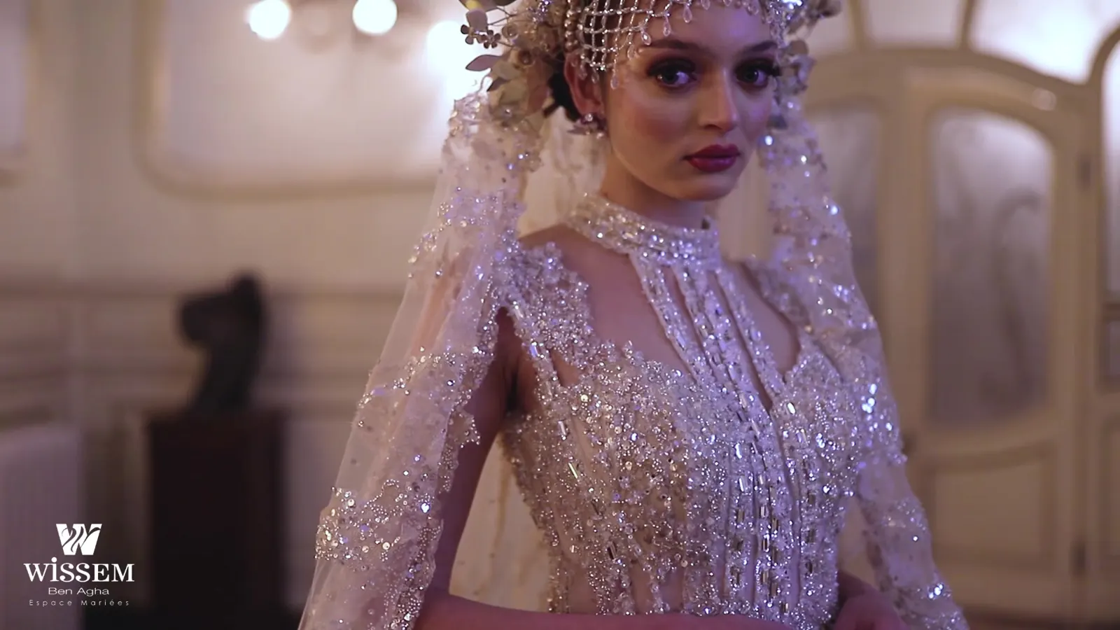 Bride standing beside carved doors wearing a beaded gown, crown headpiece and long veil