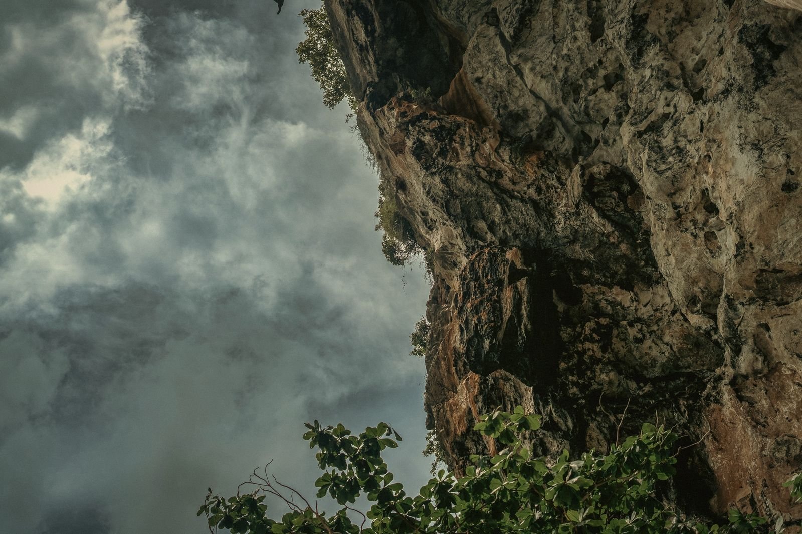 An overhanging limestone cliff under storm clouds in Krabi