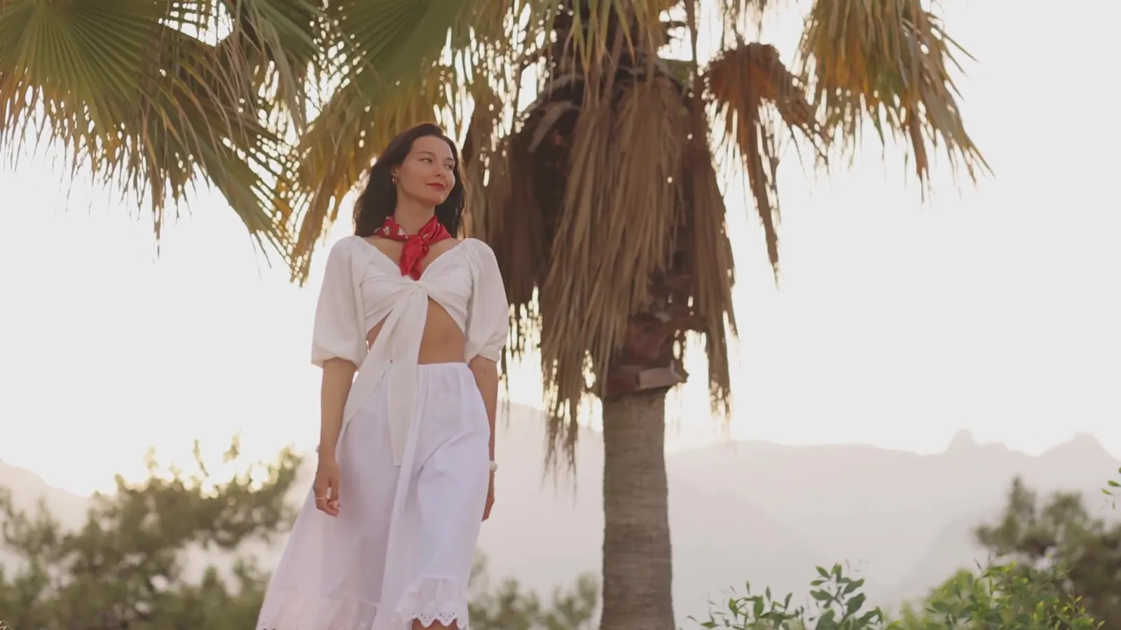 Brand film & video production, Doha studio work: woman in a white linen outfit under palm trees, opening frame of the Maya Paris campaign film