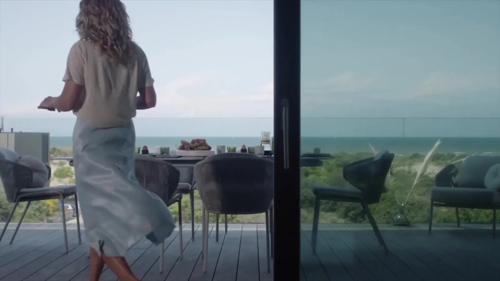 Woman in a long skirt walking across a terrace towards the sea, still from the Maya Paris campaign film