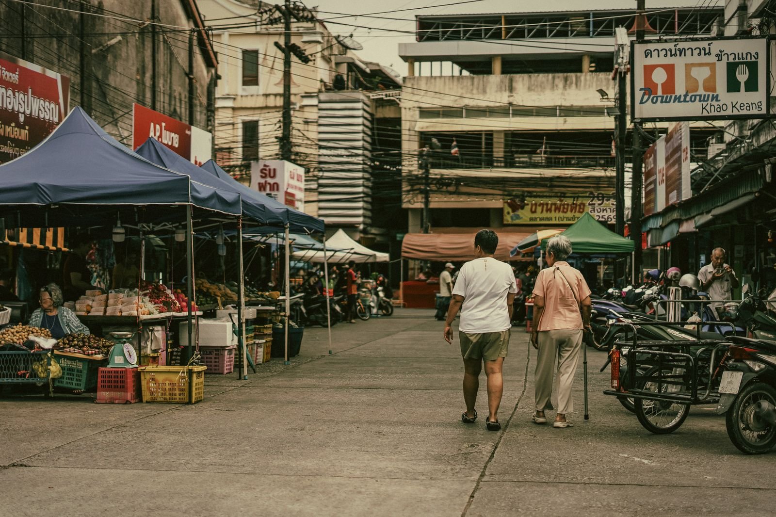 Market tents and an older couple walking a quiet street in Phuket Town