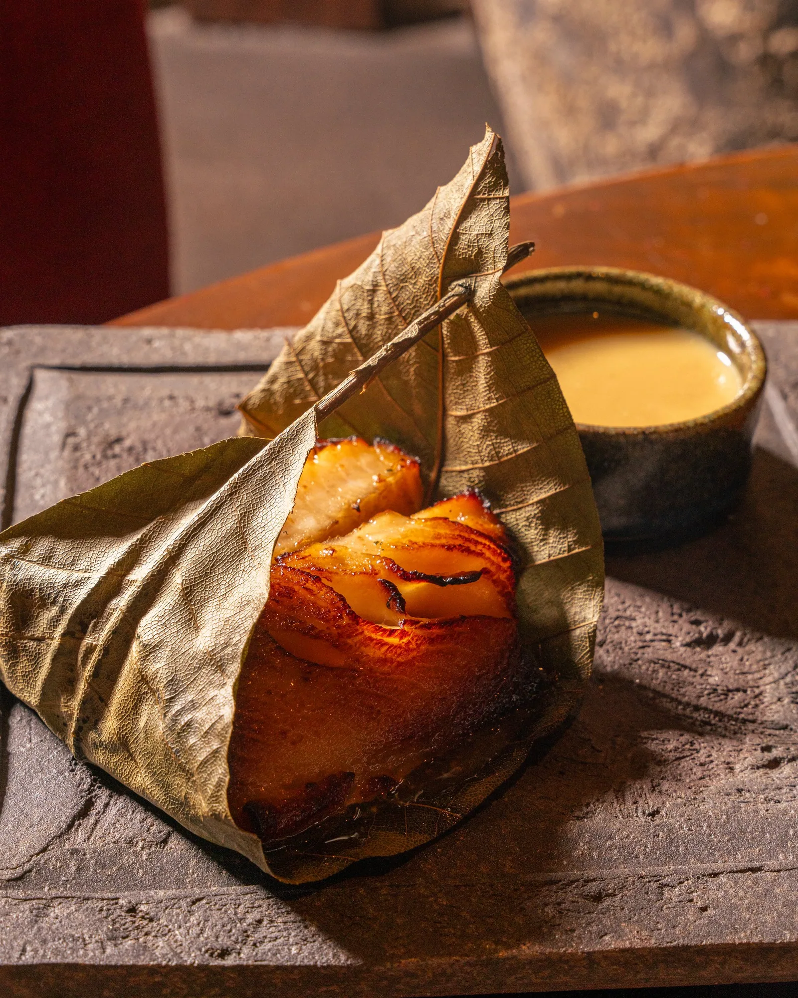 Black cod on a hoba leaf from the Zuma Doha Yashoku Night Brunch menu, lit to show the gloss of the miso glaze